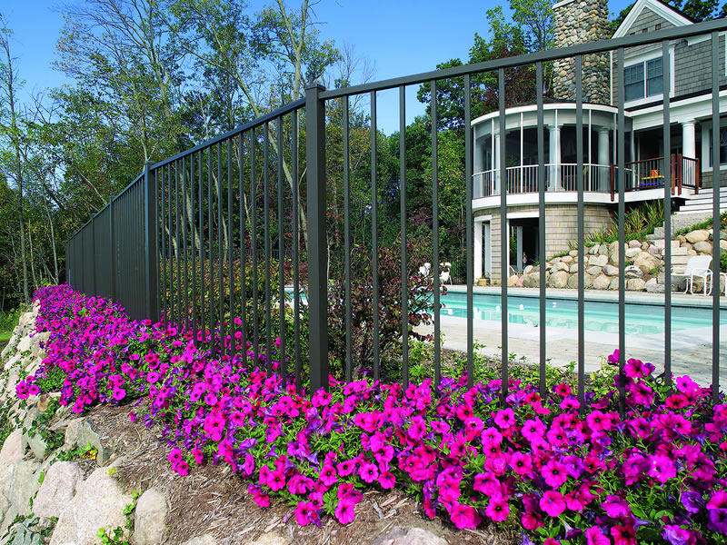 Black matte ornamental aluminum from Ultra Fence sits behind beautiful pruple flowers and a new stone patio.