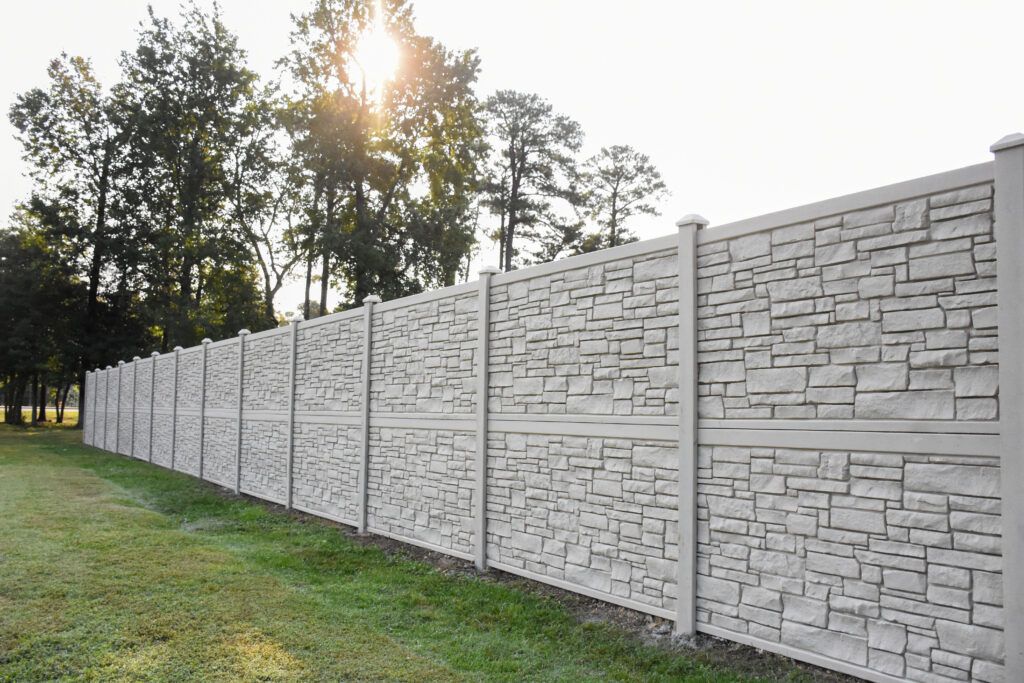 A composite fence made to look like stone with tall trees in the background.