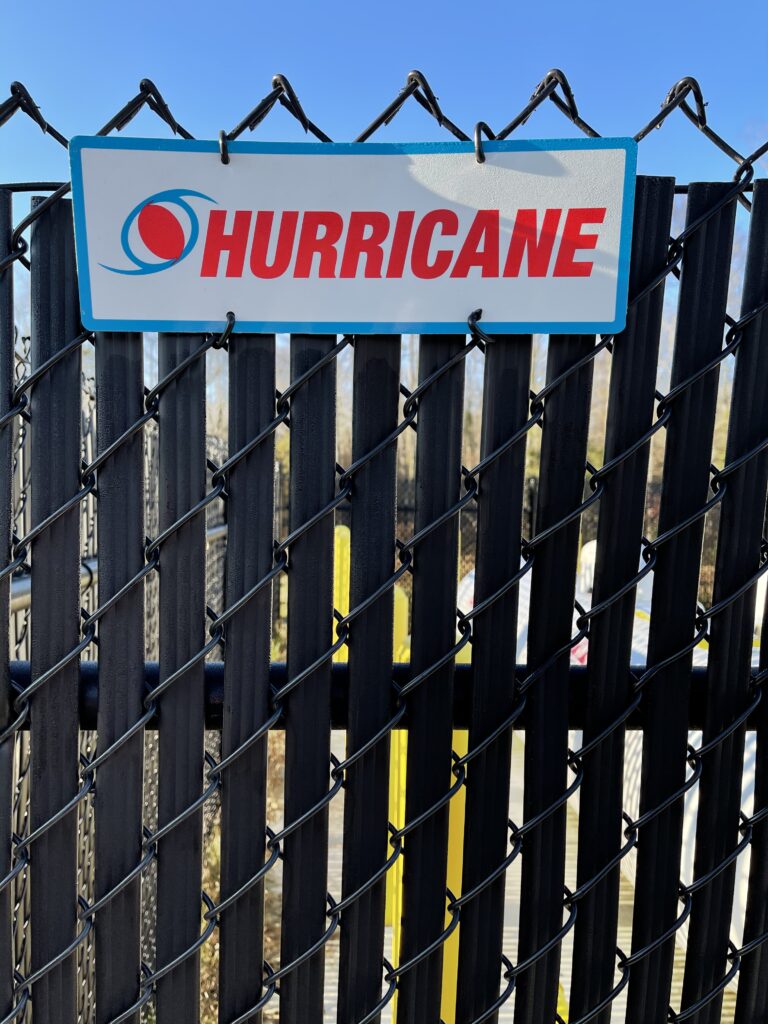 A black chain link fence with a Hurricane Fence Company sign attached to the top