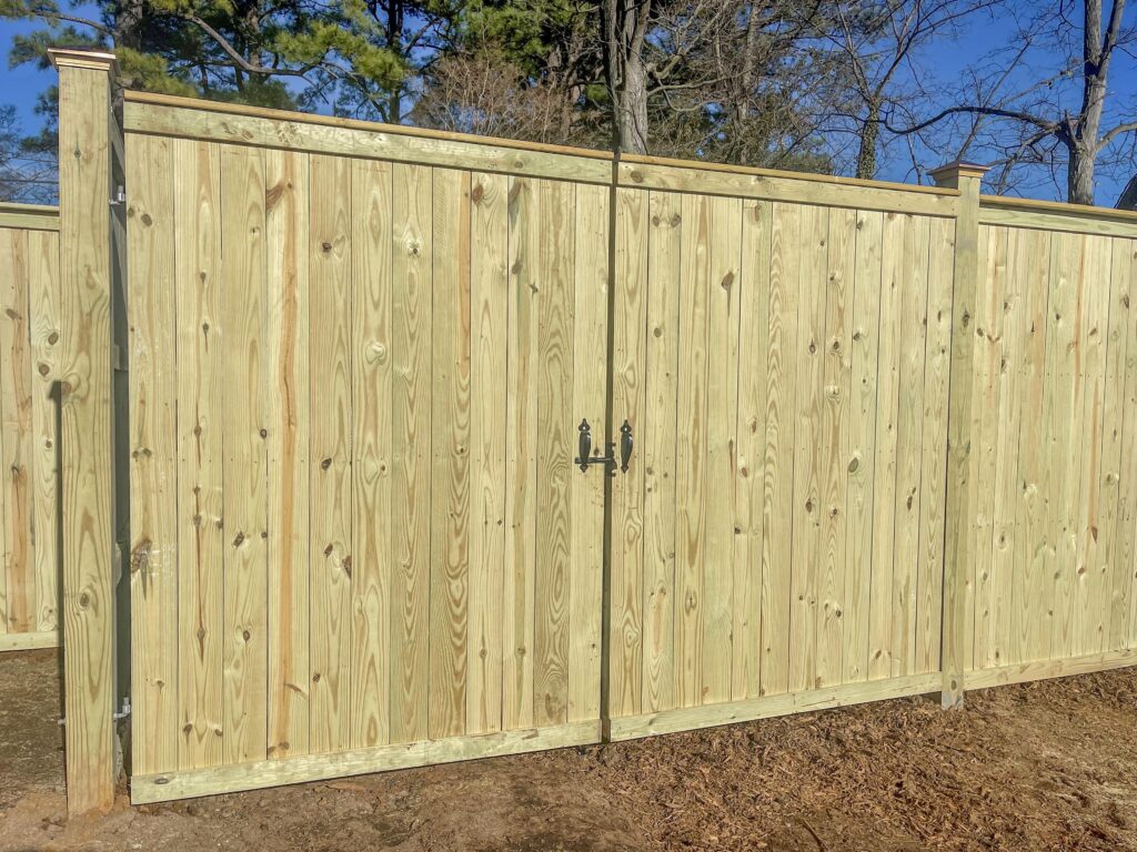 A large wooden double drive gate attached to a residential fence line.