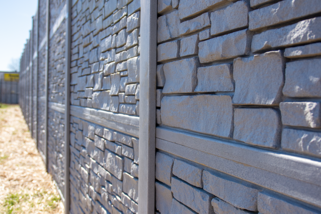 A residential composite fence with a stone finish lining the backyard of a home.